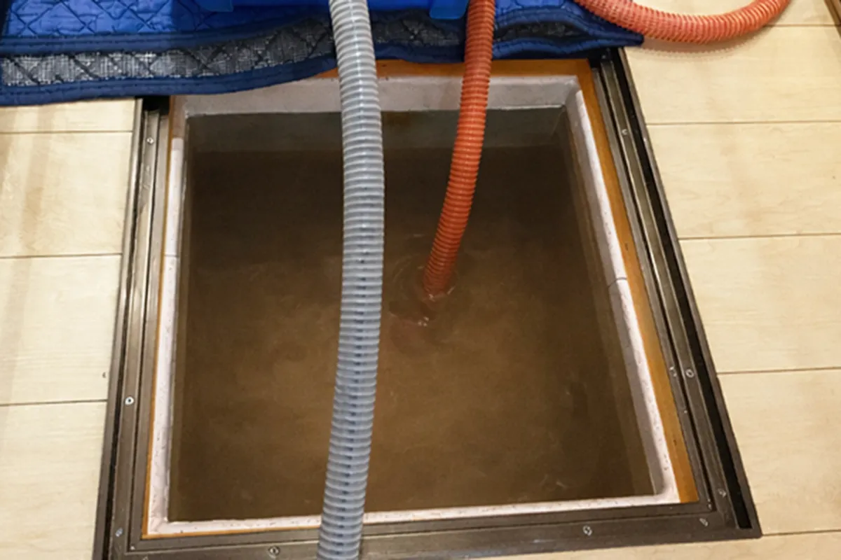 吸水ホースの先端を床下の水の中に入れる作業