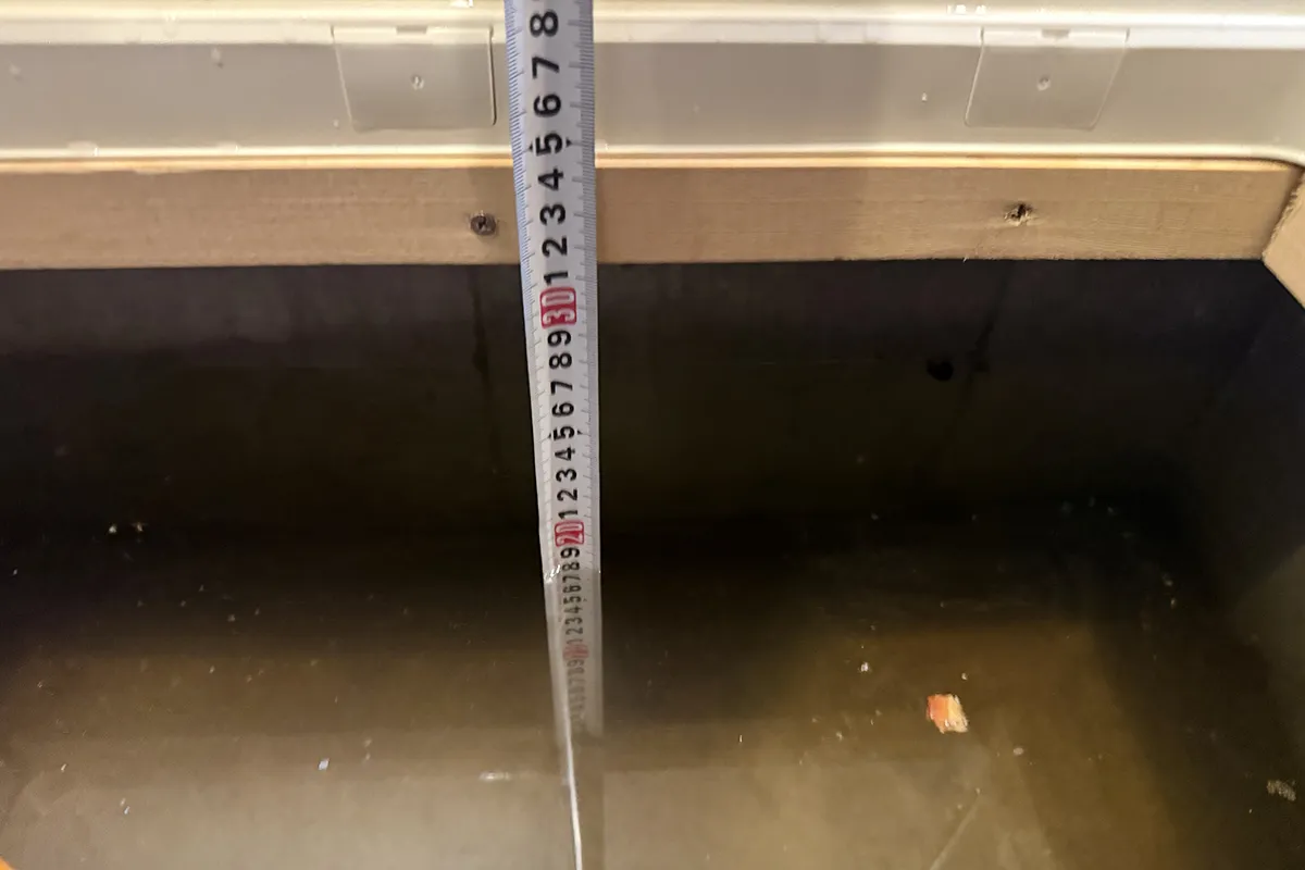 スマートフォンで床下浸水の被害状況をメジャーを当てながら撮影している様子
