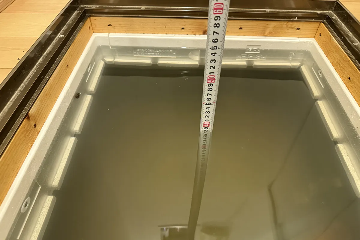 床下にメジャーを差し入れて水位を計測している写真